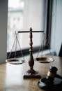 Decorative judgement scale and gavel placed on desk in light lawyer office against window